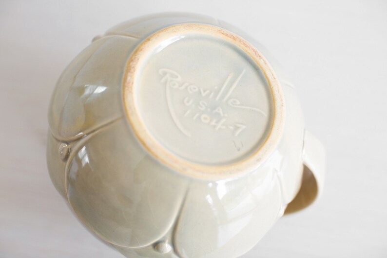 May include: A light gray ceramic bowl with a floral design. The bottom of the bowl has the text "Rareville U.S.A. 11044-7" printed on it.