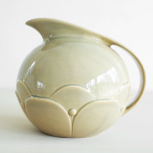 May include: A light green ceramic pitcher with a rounded body and a scalloped design. The pitcher has a handle and a spout.