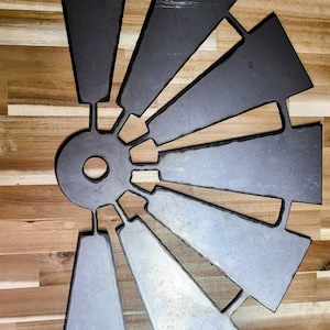 May include: A metal windmill wall decor with a silver finish and a circular center. The windmill has 12 blades that are arranged in a circular pattern.