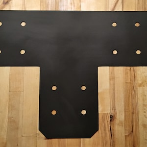 May include: Black metal T-shaped bracket with multiple holes for attaching to wood. The bracket is designed for structural support.