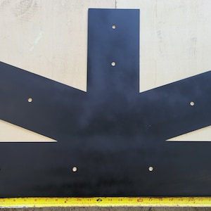 May include: A black metal truss plate with a T-shape design, featuring pre-drilled holes for fasteners. A yellow measuring tape shows the length of the plate. The plate is designed for structural support in construction projects.