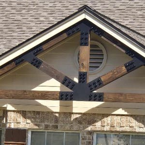 May include: A wooden beam with black metal brackets and decorative bolts. The beam is attached to a house with a light brown exterior and a gray roof.