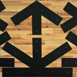 May include: A set of eight black metal corner braces, arranged in a pattern on a wooden surface. The braces are designed to reinforce corners and joints in woodworking projects.