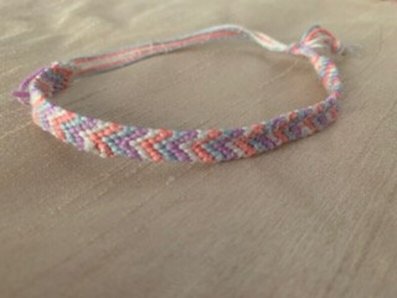 May include: A friendship bracelet with a chevron pattern in pink, purple, and white.