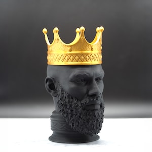May include: A black bust sculpture of a man wearing a gold crown. The man has a beard and a serious expression.