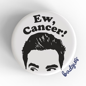 Peut inclure: Un badge blanc avec le texte "Ew, Cancer!" en noir, au-dessus d'une illustration en noir et blanc des cheveux et des yeux d'une personne. Le mot "badgies" est écrit en bleu en cursive.