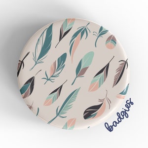 May include: A round phone grip with a white background and a pattern of colorful feathers. The text "badgirls" is written in blue on the bottom of the grip.