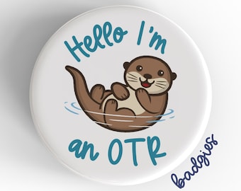 May include: A white button with a blue and brown cartoon otter floating on its back in water. The text "Hello I'm an OTR" is written in blue on the button.