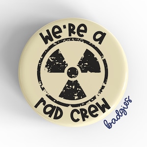May include: A cream-colored button with a black and white radiation symbol and the text "We're a rad crew".