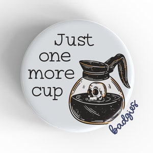 May include: White button with black text that reads "Just one more cup" and a black and white illustration of a coffee pot with a skull inside. The text "badgriss" is written in blue below the illustration.
