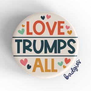 May include: A round button with a cream background and colorful hearts. The text "LOVE TRUMPS ALL" is written in bold, colorful letters.
