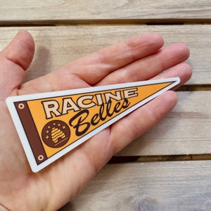 May include: A yellow and brown pennant with the text "RACINE Belles" and a beehive design.