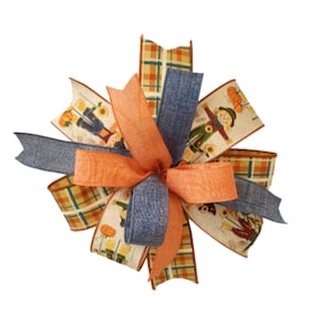 May include: A decorative fall-themed bow featuring a mix of orange, blue, and plaid ribbons. The bow has a central orange ribbon and is adorned with ribbons printed with scarecrows, pumpkins, and sunflowers. Perfect for autumn decor.