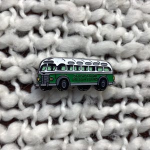 May include: Green and white enamel pin of a bus with the text "Shawshank Prison Tours".