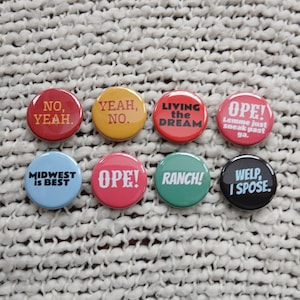 May include: A collection of eight round buttons with various phrases in white text on different colored backgrounds. The buttons include phrases like "NO, YEAH," "YEAH, NO," and "LIVING the DREAM."