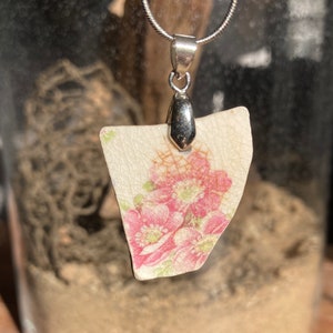 May include: A silver chain necklace with a pendant made from a piece of vintage china with a floral pattern in shades of pink and green.