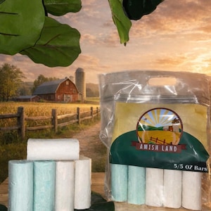 May include: A clear plastic package of Amish Land 5/5 OZ Bars with a farm scene label. Several cylindrical bars, some white and some light blue, are arranged on a leaf. A rural landscape with a red barn is in the background.