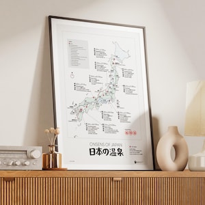 Puede incluir: Impresión enmarcada del mapa titulada "ONSENS OF JAPAN" con texto en japonés. El mapa destaca ubicaciones en Japón, con una leyenda y varios iconos. La impresión está en un marco negro, exhibida en un mueble de madera con objetos decorativos.