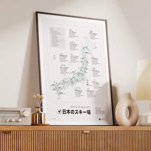 May include: Framed map print titled "Japan Ski Resorts" with a detailed illustration of ski areas across Japan. The map features a white background with black and blue lines, and text in English and Japanese. The print is displayed on a wooden cabinet.