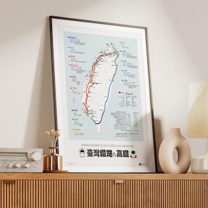 May include: Framed map print of the Taiwan Railway & High Speed Rail Network. The map shows rail routes across Taiwan, with text in English and Chinese. The print is displayed on a wooden cabinet, with a vase and lamp.