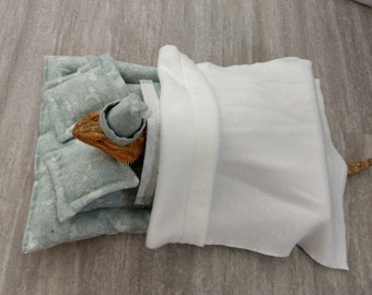 May include: A bearded dragon wearing a blue and white sleep cap is tucked into a light blue and white patterned bedding set with a white blanket.