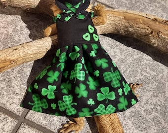 May include: A black and green dress with shamrock print and a black hat with a green shamrock trim. The dress is worn by a lizard.