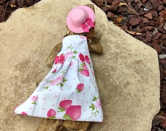 May include: A small reptile wearing a pink hat and a white dress with pink polka dots and strawberry print.