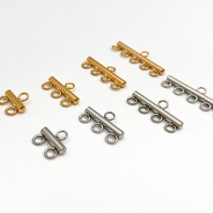 May include: A set of gold and silver metal connector pieces for jewelry making. The pieces have multiple loops for attaching chains or cords.