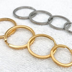 May include: A set of six key rings, three gold and three silver, arranged in a circle on a white surface. The key rings are different sizes and are linked together.