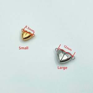May include: Two gold-tone heart-shaped magnetic clasps for jewelry making. The smaller clasp measures 8.5 mm and the larger clasp measures 12 mm.