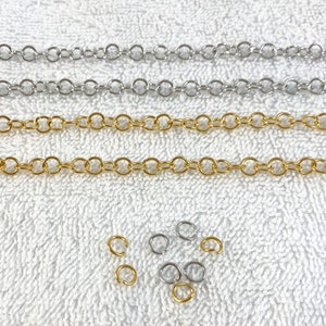 May include: Three strands of chain, one gold and two silver, laid out on a white surface. There are also several small jump rings in both gold and silver.