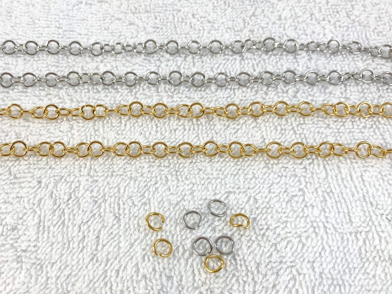 May include: Three strands of chain, one gold and two silver, laid out on a white surface. There are also several small jump rings in both gold and silver.