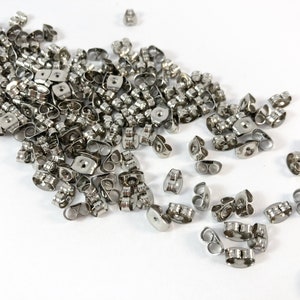 May include: A large quantity of silver-toned earring backs. The backs are made of metal and have a small loop on each side. They are designed to be used with post earrings.