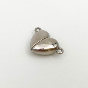 May include: Silver heart-shaped magnetic clasp for jewelry making. The clasp has two loops for attaching to a necklace or bracelet.