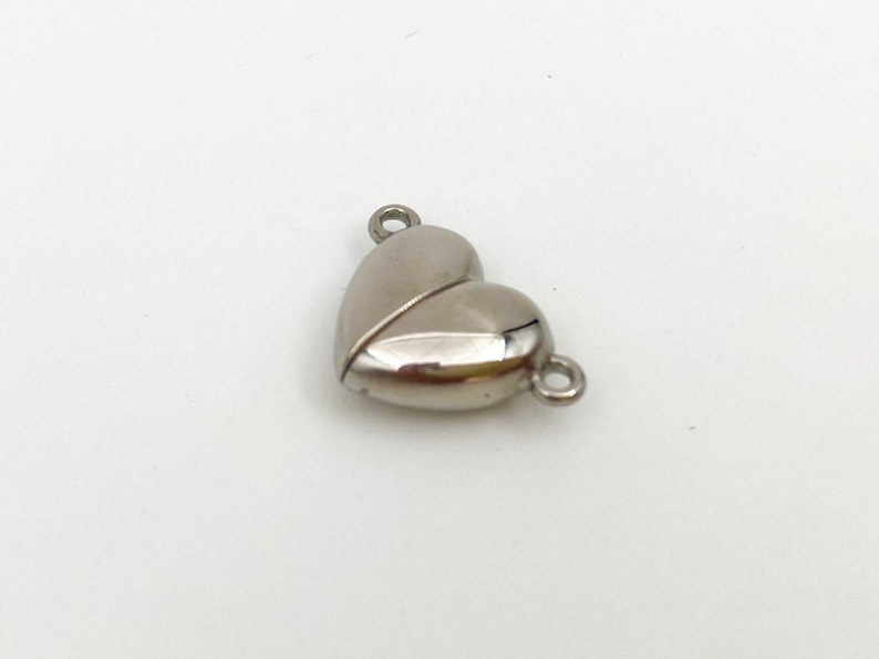 May include: Silver heart-shaped magnetic clasp for jewelry making. The clasp has two loops for attaching to a necklace or bracelet.