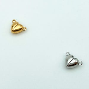 May include: Two heart-shaped magnetic clasps for jewelry making. One is gold and the other is silver.