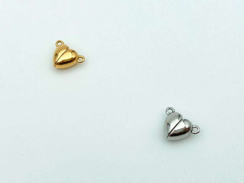 May include: Two heart-shaped magnetic clasps for jewelry making. One is gold and the other is silver.