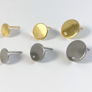 May include: Four pairs of earring findings, two gold and two silver. Each finding is a round disc with a small hole in the center.
