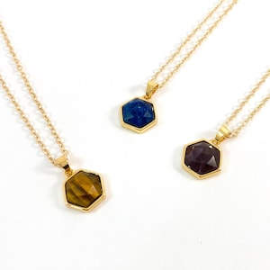 May include: Three gold necklaces with hexagonal pendants featuring different colored gemstones. The pendants are blue, purple, and brown.