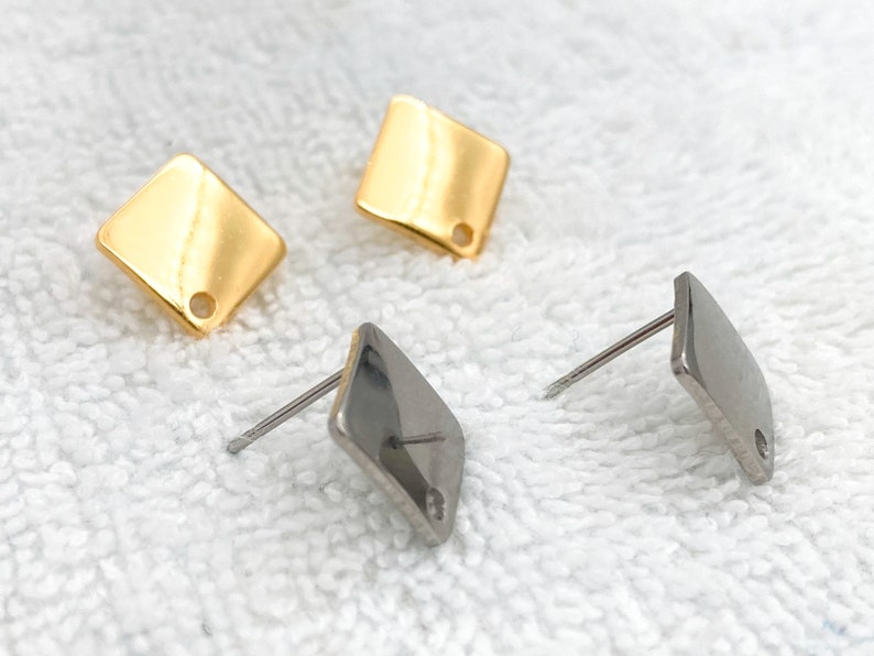 May include: Two pairs of earrings, one gold and one silver. Both earrings are square shaped with a small hole in the centre.