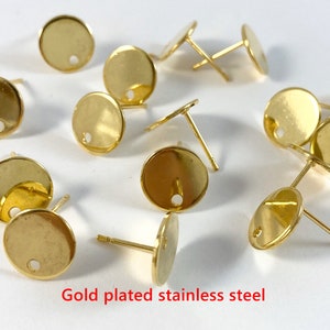 May include: A close-up of gold-plated stainless steel earring findings. The findings are round with a small hole in the center. They are perfect for making your own earrings.