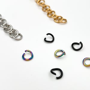 May include: A close-up of various jump rings in different colors and finishes. The jump rings are silver, gold, black, and rainbow.