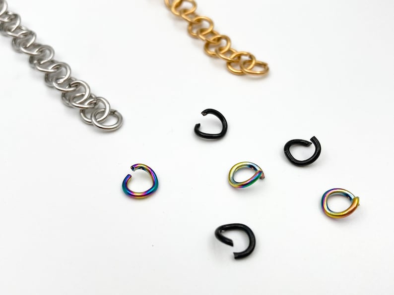 May include: A close-up of various jump rings in different colors and finishes. The jump rings are silver, gold, black, and rainbow.