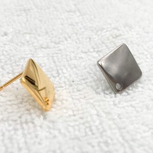 May include: Two square-shaped earrings, one gold and one silver, with a small hole in the centre of each.