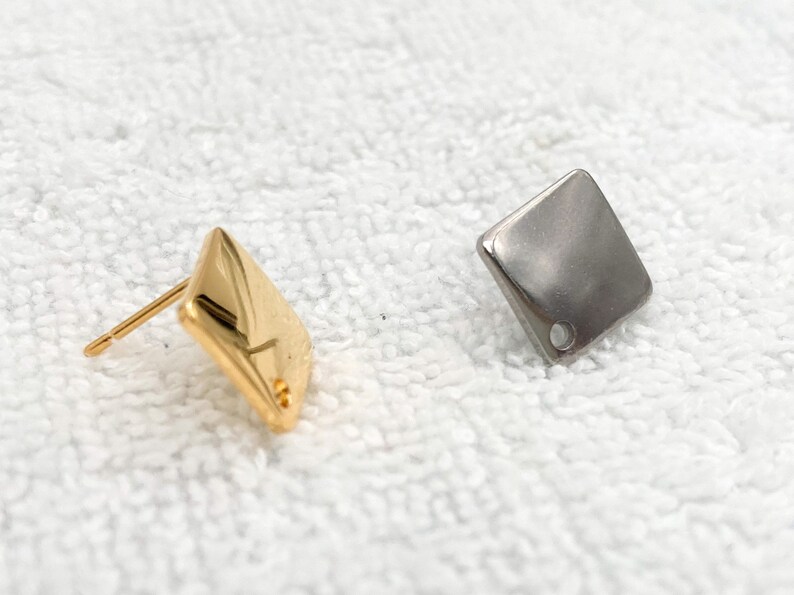 May include: Two square-shaped earrings, one gold and one silver, with a small hole in the centre of each.