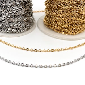 May include: Two spools of chain, one silver and one gold, with a length of each chain laid out in front of the spools. The chain is a delicate, round link style.