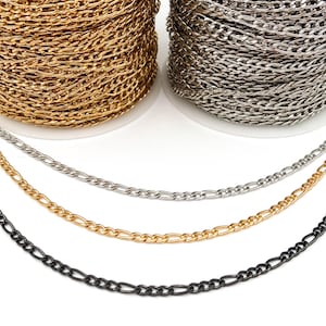 May include: Three chains of different colors: black, gold, and silver. The chains are laid out in a row, with the black chain on the bottom, the gold chain in the middle, and the silver chain on top. The chains are all the same style, with a flat, oval-shaped link.