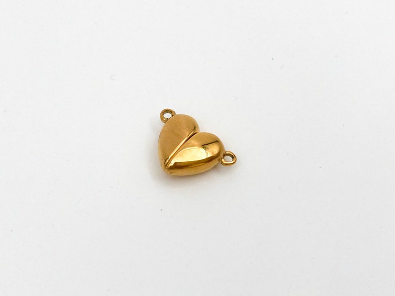 May include: A gold-colored heart-shaped charm with two loops for attaching to a necklace or bracelet.