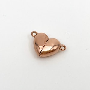 May include: A rose gold heart-shaped magnetic clasp for jewelry making. The clasp is made of metal and has a shiny finish.