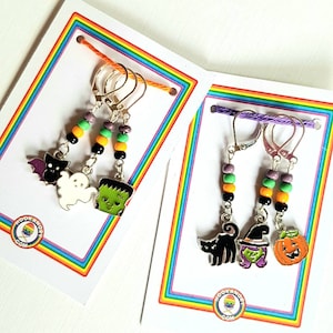 May include: Three sets of Halloween themed stitch markers with colorful beads and charms. The charms include a ghost, a monster, a bat, a cat, a pumpkin, and a witch's hat.